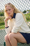 Ivory | Woman wearing the Jenny Knit Crewneck sitting on a bench with a green fence in the background