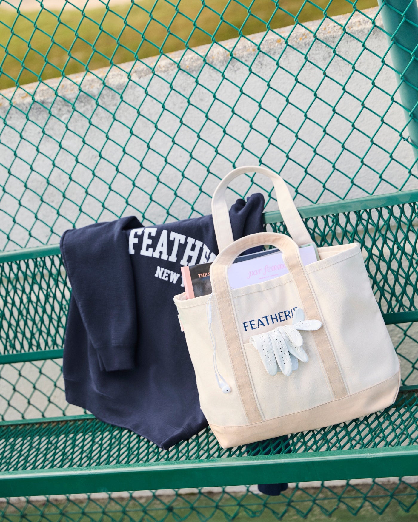 Navy sweatshirt and beige tote bag with FEATHERIE branding on a green metal bench.