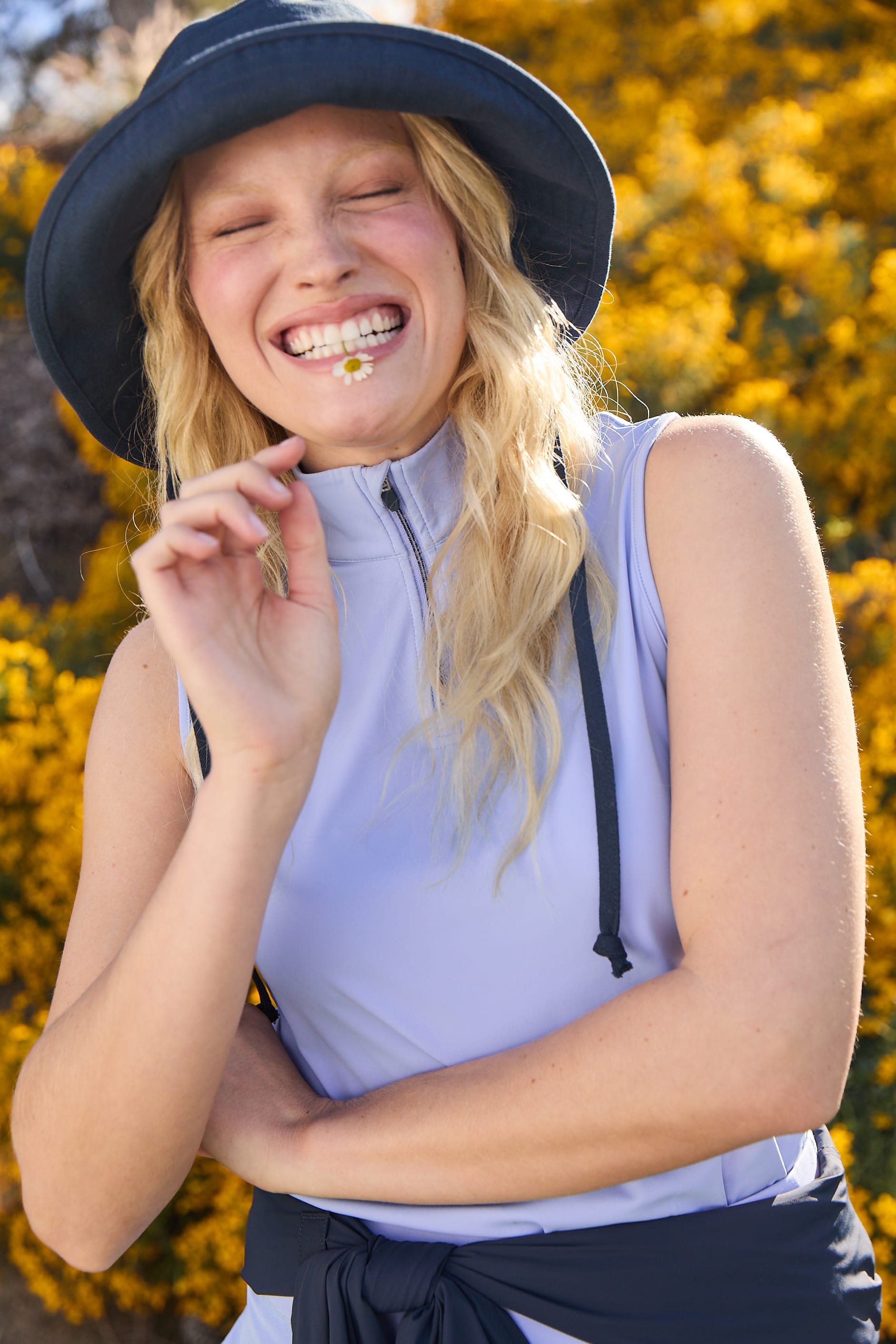 Woman wearing a blue hat and sleeveless top with a blurred yellow flower background