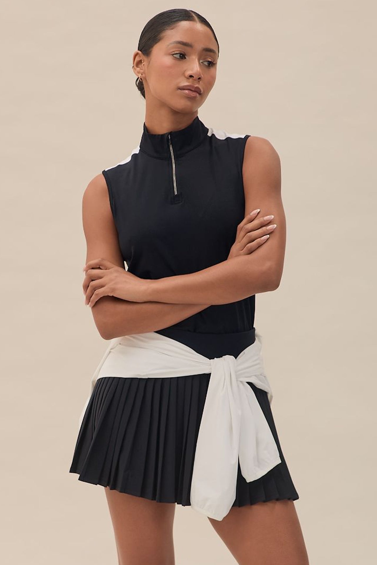 A model wearing a black sleeveless top mid-waist black skort with integrated moisture-wicking knit short, designed for golf ball storage and tee holders.