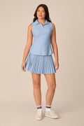 Skyline | A woman modeling a light blue sleeveless polo shirt and matching pleated skirt set, paired with white socks and white sneakers, against a solid beige studio background.