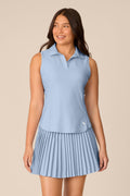 Skyline | A woman modeling a light blue sleeveless polo shirt with a matching pleated mini skirt against a solid beige background.