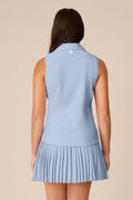 Skyline | A woman shown from the back wearing a light blue sleeveless collared top and matching pleated mini skirt against a plain beige studio background.