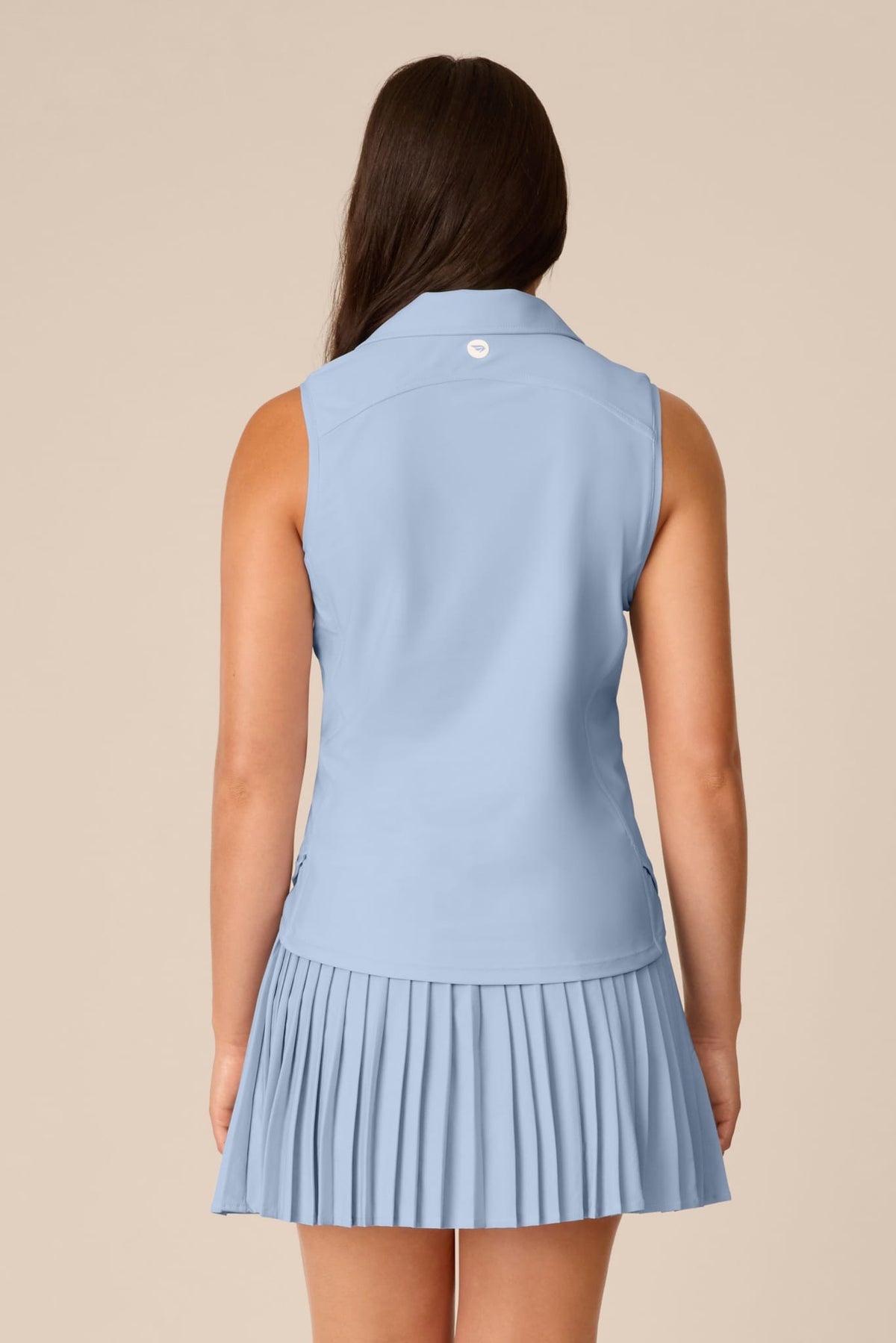 Skyline | A woman shown from the back wearing a light blue sleeveless collared top and matching pleated mini skirt against a plain beige studio background.