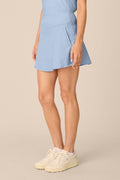 Skyline | A model wearing a light blue athletic mini skirt with side pockets and cream-colored sneakers, shown from the waist down against a solid beige background.