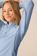 Skyline | A woman wearing a light blue long-sleeve athletic quarter-zip pullover, shown from the chest up against a plain beige studio background.
