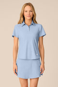 Skyline | A woman modeling a light blue short-sleeve polo shirt and matching mini skirt against a solid beige background.