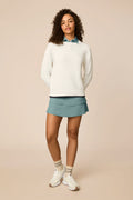 Ivory | Woman wearing The Jenny Knit Crewneck beige sweater, tulip skort, and white sneakers on a beige background