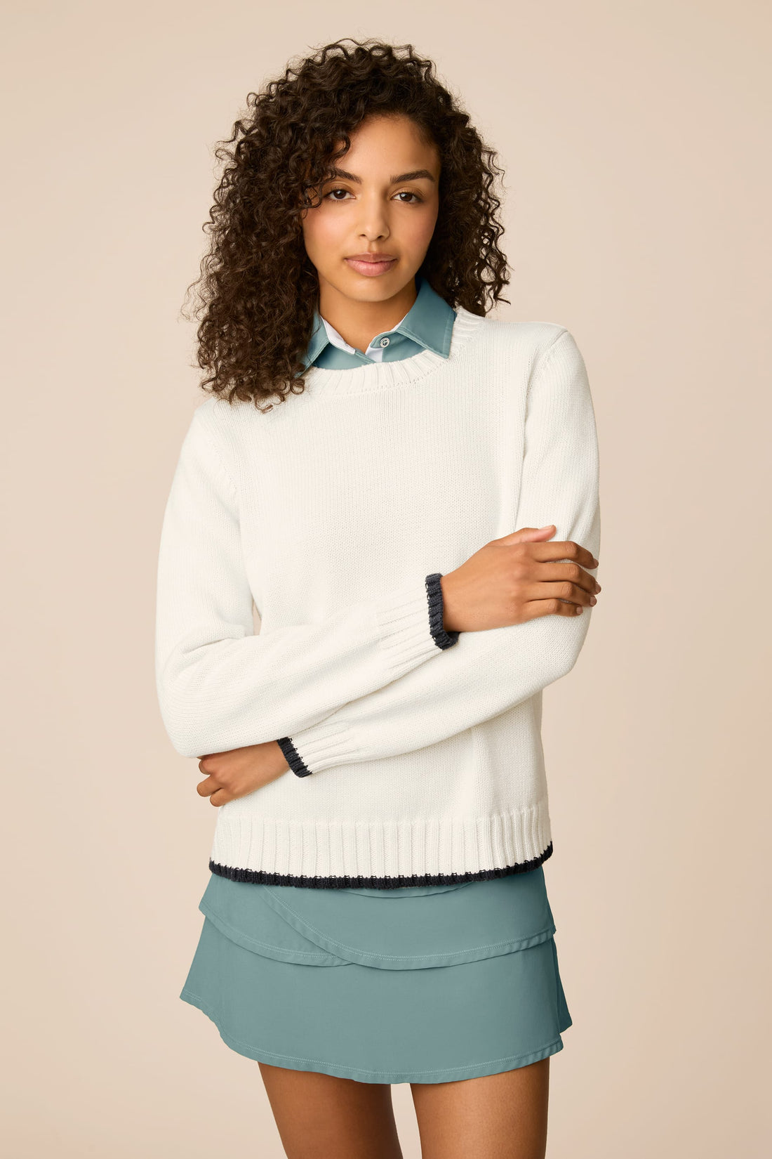 Ivory | Woman wearing a beige The Jenny Knit Crewneck sweater over a blue shirt with a light blue skirt on a beige background