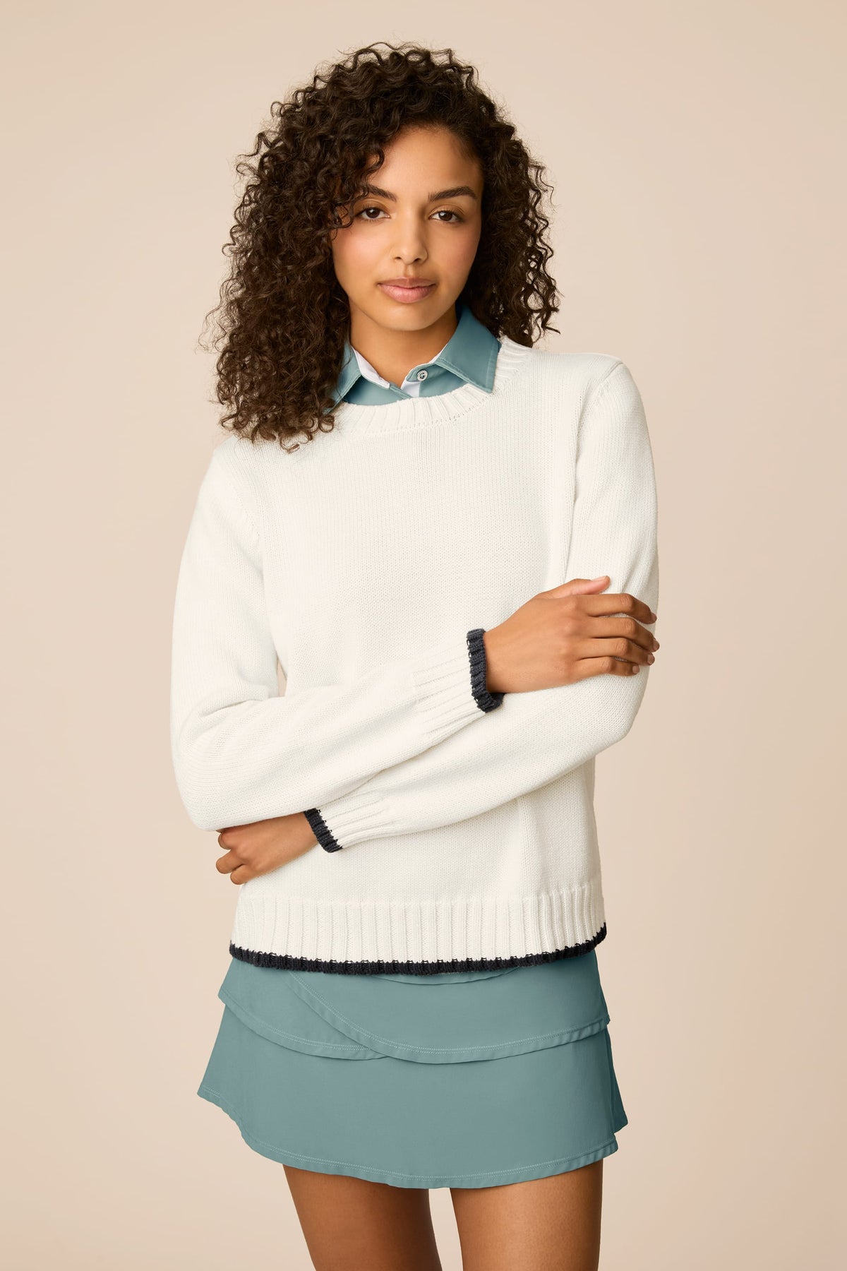 Ivory | Woman wearing a beige The Jenny Knit Crewneck sweater over a blue shirt with a light blue skirt on a beige background