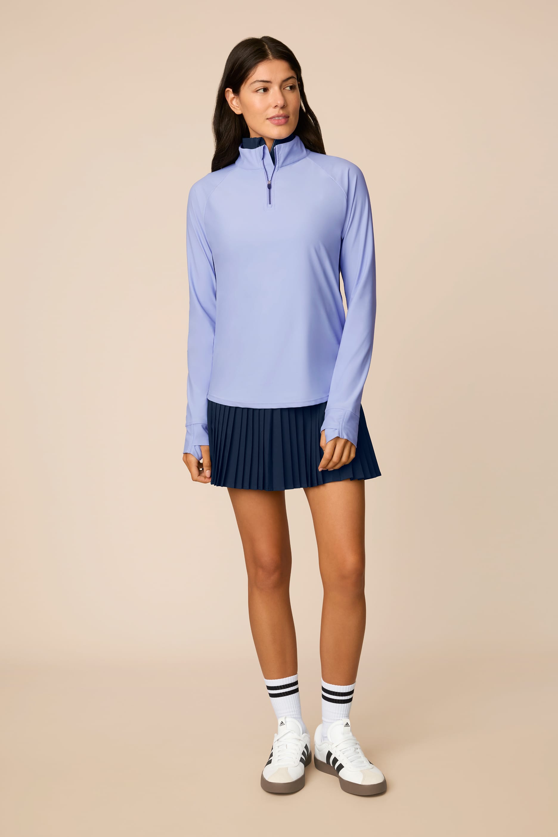 Woman wearing a Stardust long-sleeve half-zip top and dark pleated skirt on a beige background