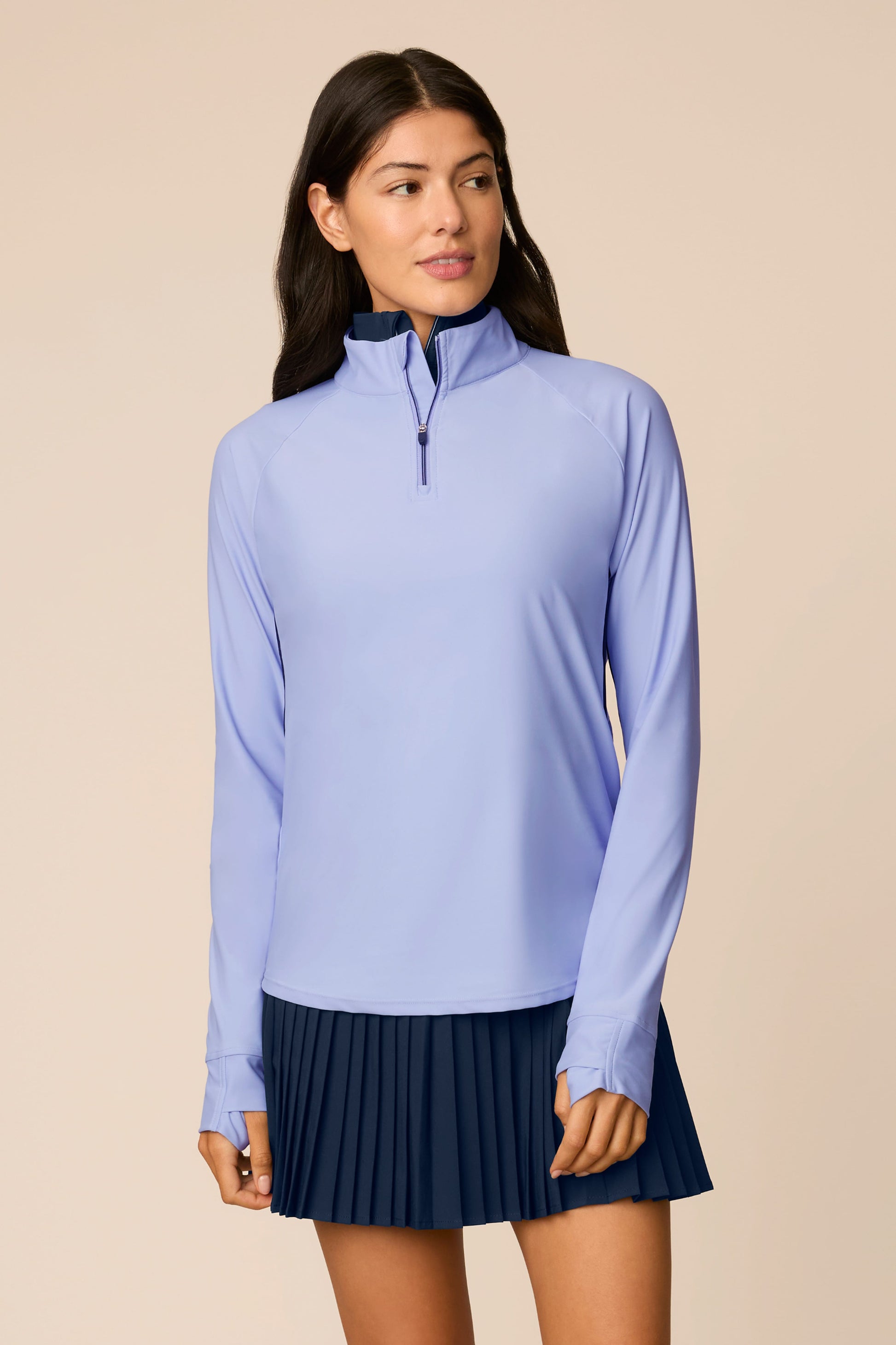 Woman wearing The Taylor Long-Sleeve Half-Zip and navy pleated skirt on a beige background