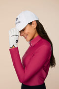 Aurora | Woman wearing The Ella Long Sleeve Polo and white cap on a beige background
