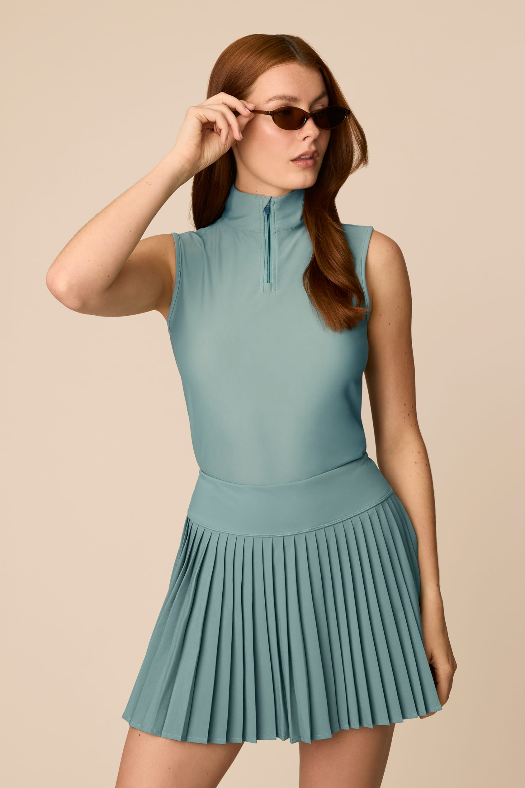 Meadow Haze | Woman wearing a Meadow Haze colored sleeveless top with a zipper on a beige background