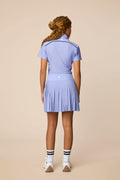 Stardust | Junior golfer wearing a Stardust color Lexi polo shirt and pleated skirt on a beige background