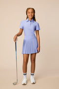 Stardust | Junior golfer wearing a Stardust color Lexi polo shirt and pleated skirt on a beige background