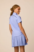 Stardust | Junior golfer wearing a Stardust color Lexi polo shirt and pleated skirt on a beige background