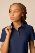 Midnight | Junior golfer wearing a Midnight color Lexi polo shirt and pleated skirt on a beige background