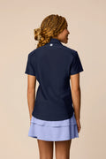 Midnight | Junior golfer wearing a Midnight color Lexi polo shirt and pleated skirt on a beige background