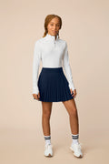 Midnight | Junior golfer wearing a Midnight color pleated skort on a beige background
