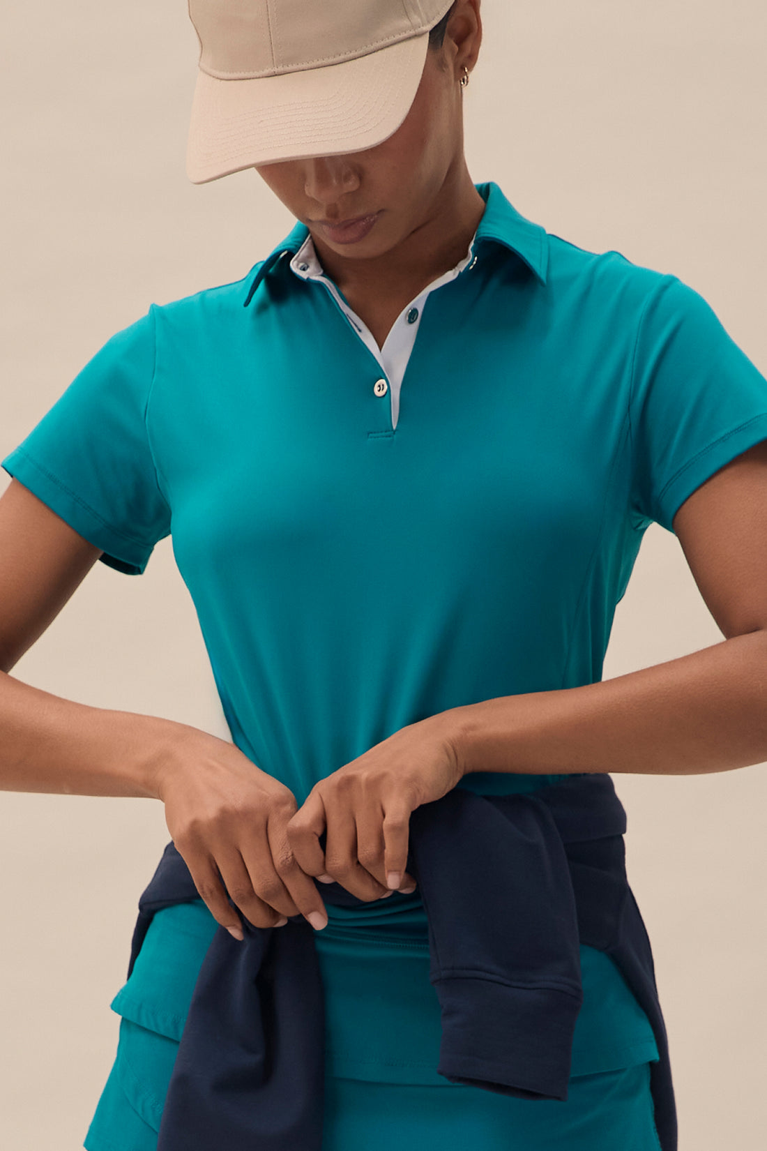 Teal | A female model wearing a teal polo shirt with a feminine fit, and a tulip hem skort, with a beige cap.