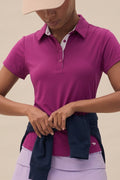 Plum | Woman wearing a plum polo shirt and beige cap with a neutral background