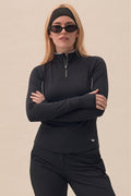 Black | Woman wearing a black quarter-zip outfit with sunglasses on a beige background