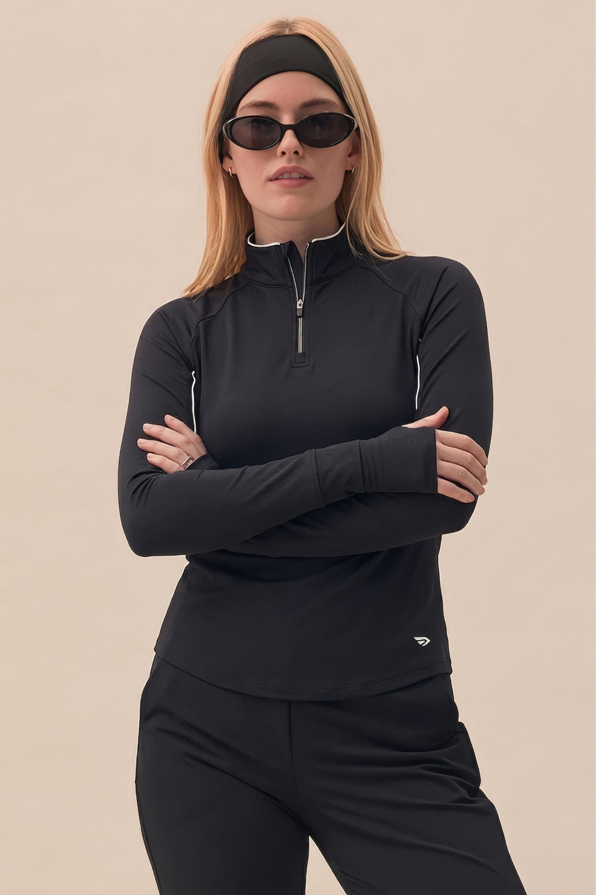 Black | Woman wearing a black quarter-zip outfit with sunglasses on a beige background