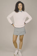 Ivory | Woman wearing The Jenny Knit Crewneck beige sweater, tulip skort, and white sneakers on a beige background