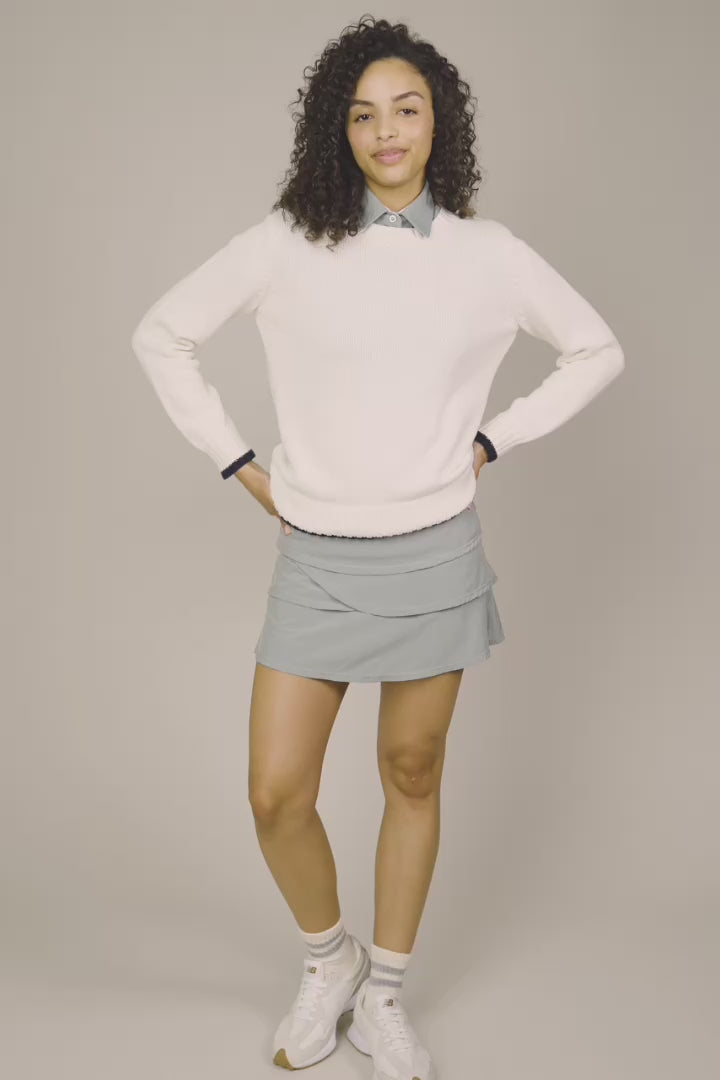 Ivory | Woman wearing The Jenny Knit Crewneck beige sweater, tulip skort, and white sneakers on a beige background
