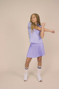 Stardust | Junior golfer wearing a Stardust color Lexi polo shirt and pleated skirt on a beige background